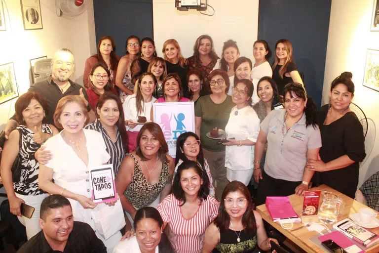 Grupo numeroso de empresarias posando en un local con el cartel de Empodérate y Emprende y el libro Conectados