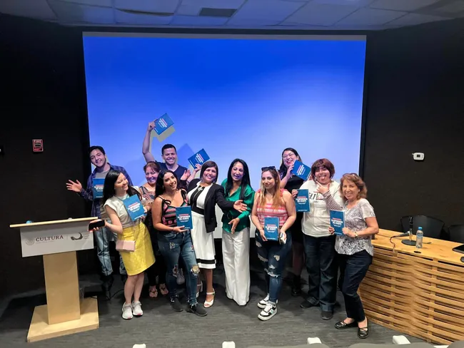 Grupo de personas sonriendo con ejemplares del libro La experiencia del cliente frente a una pantalla azul