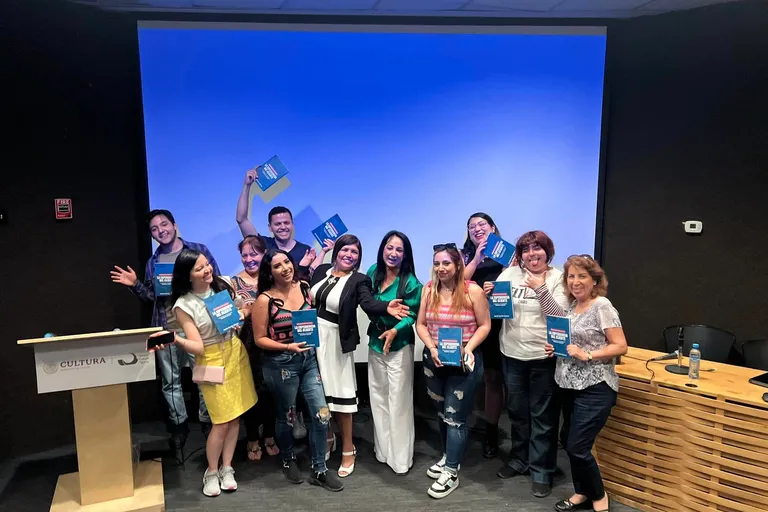 Grupo de personas sonriendo con ejemplares del libro La experiencia del cliente frente a una pantalla azul