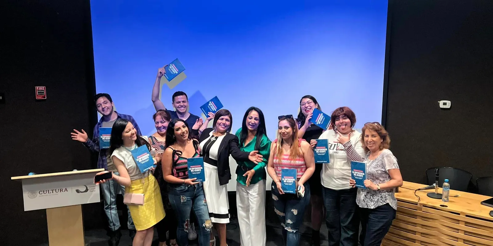 Grupo de personas sonriendo con ejemplares del libro La experiencia del cliente frente a una pantalla azul
