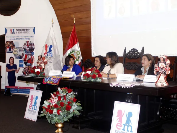 Mesa de honor del foro con cuatro mujeres sentadas, arreglos de rosas rojas y carteles de Empodérate y Emprende