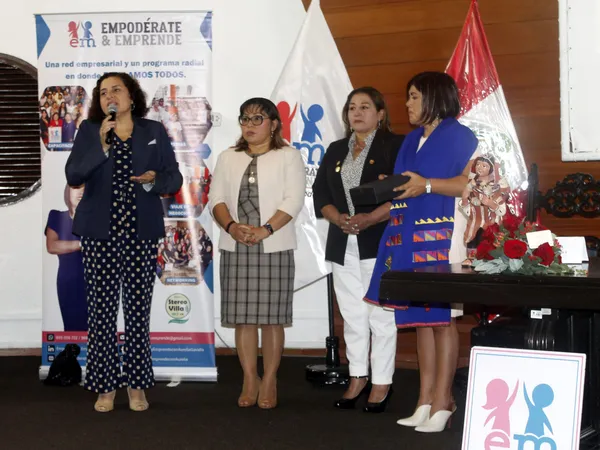 Cuatro mujeres de pie en el escenario: una habla al micrófono y otra sostiene una caja negra y una figura de cerámica