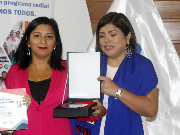 Dos mujeres posan con un certificado y una placa de reconocimiento en un estuche abierto