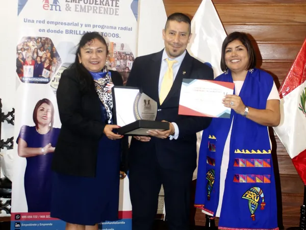 Un hombre y dos mujeres posan con una placa y un certificado frente al banner de Empodérate y Emprende