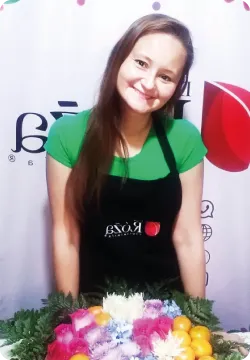 Retrato de Erika Brachowicz con delantal de D’la Róza, junto a un arreglo de flores