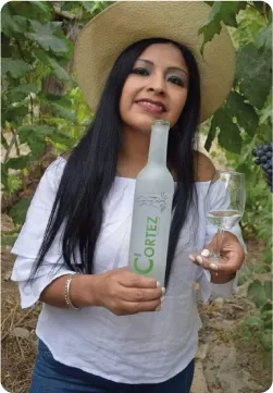 Retrato de Elizabeth Cortez Martinez con una botella de Pisco Don Cortez en un viñedo