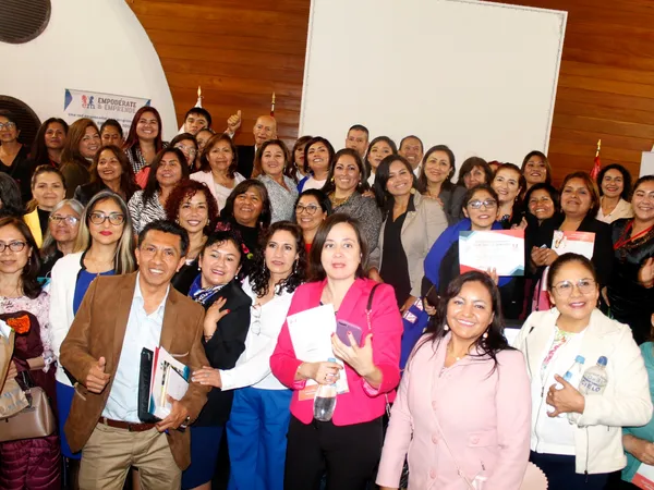 Numeroso grupo de empresarias y empresarios posando juntos en un auditorio de paredes de madera, algunos con diplomas